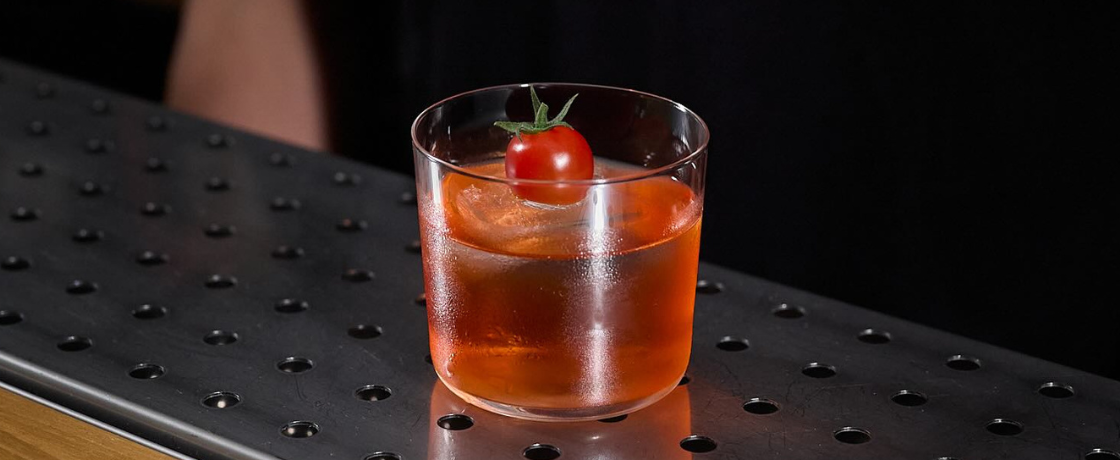 Un cocktail di colore rosso con un pomodorino come decorazione