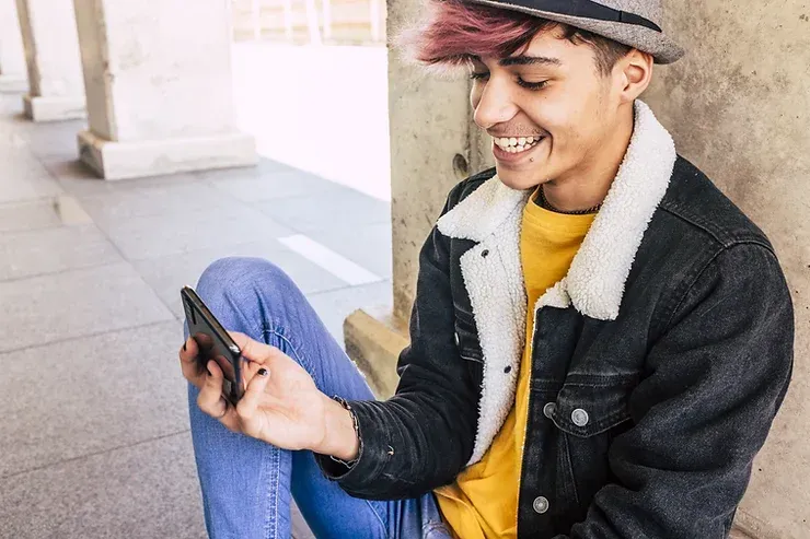 A young person is sitting on the ground looking at their phone.