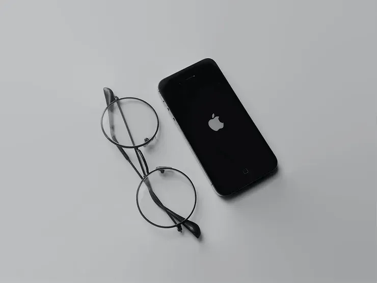A pair of glasses resting next to an Apple iPhone