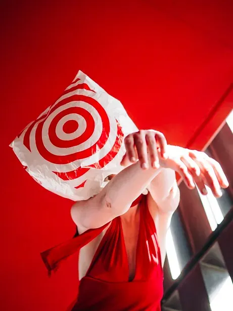 A woman in a red dress with a pillow on her head that has a target on it