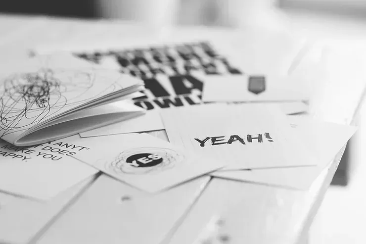 Una foto in bianco e nero di una pila di carte su un tavolo, con sopra schizzi e sketch che sembrano essere fatti a penna.