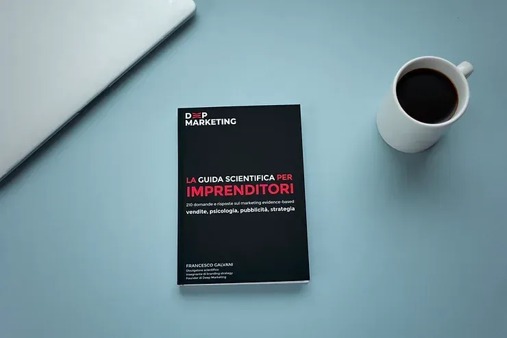 Un libro è appoggiato su un tavolo accanto a una tazza di caffè e un computer portatile.